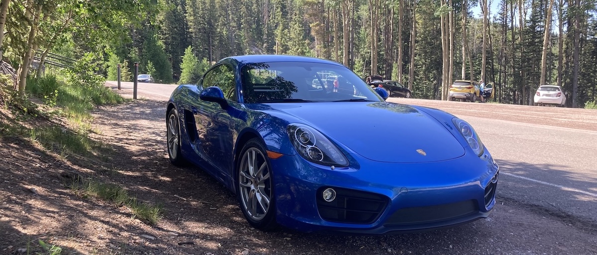 A blue Porsche Cayman driving on a mountain road