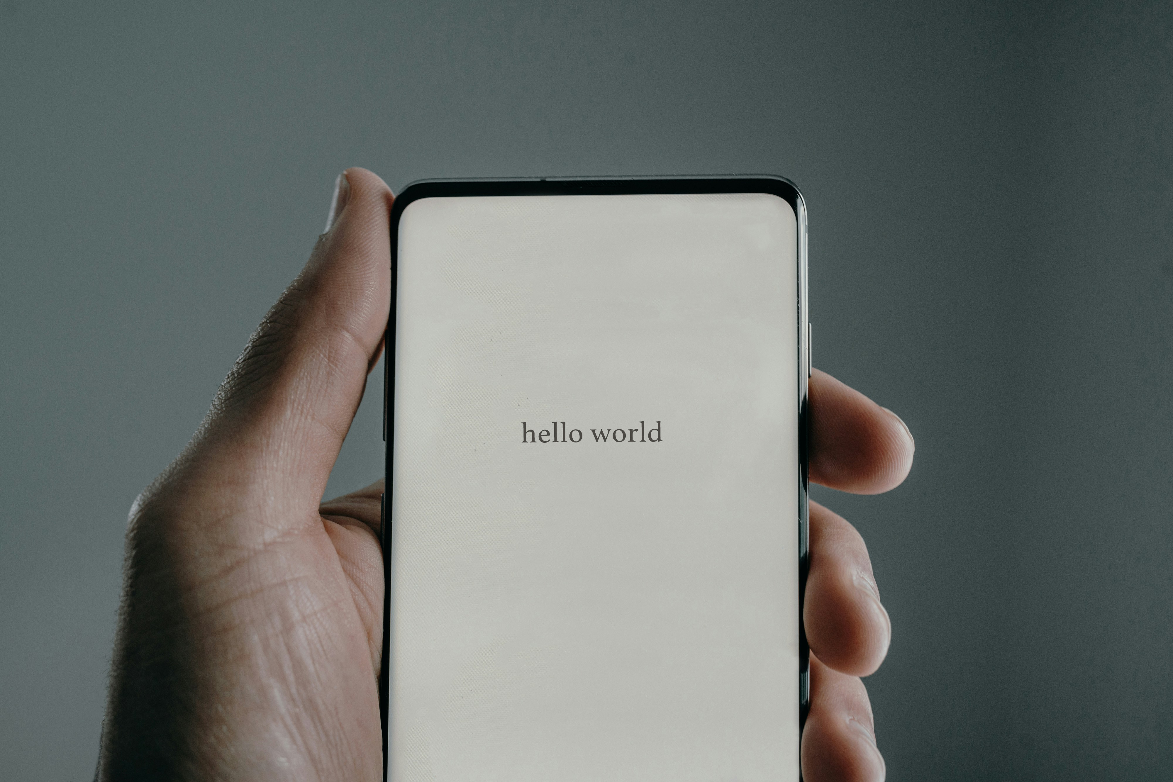A hand holding a smartphone that says 'hello world'